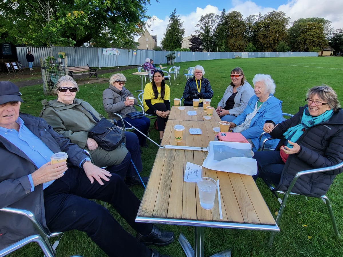 A group of people sitting at a table in a field having some drinks. 