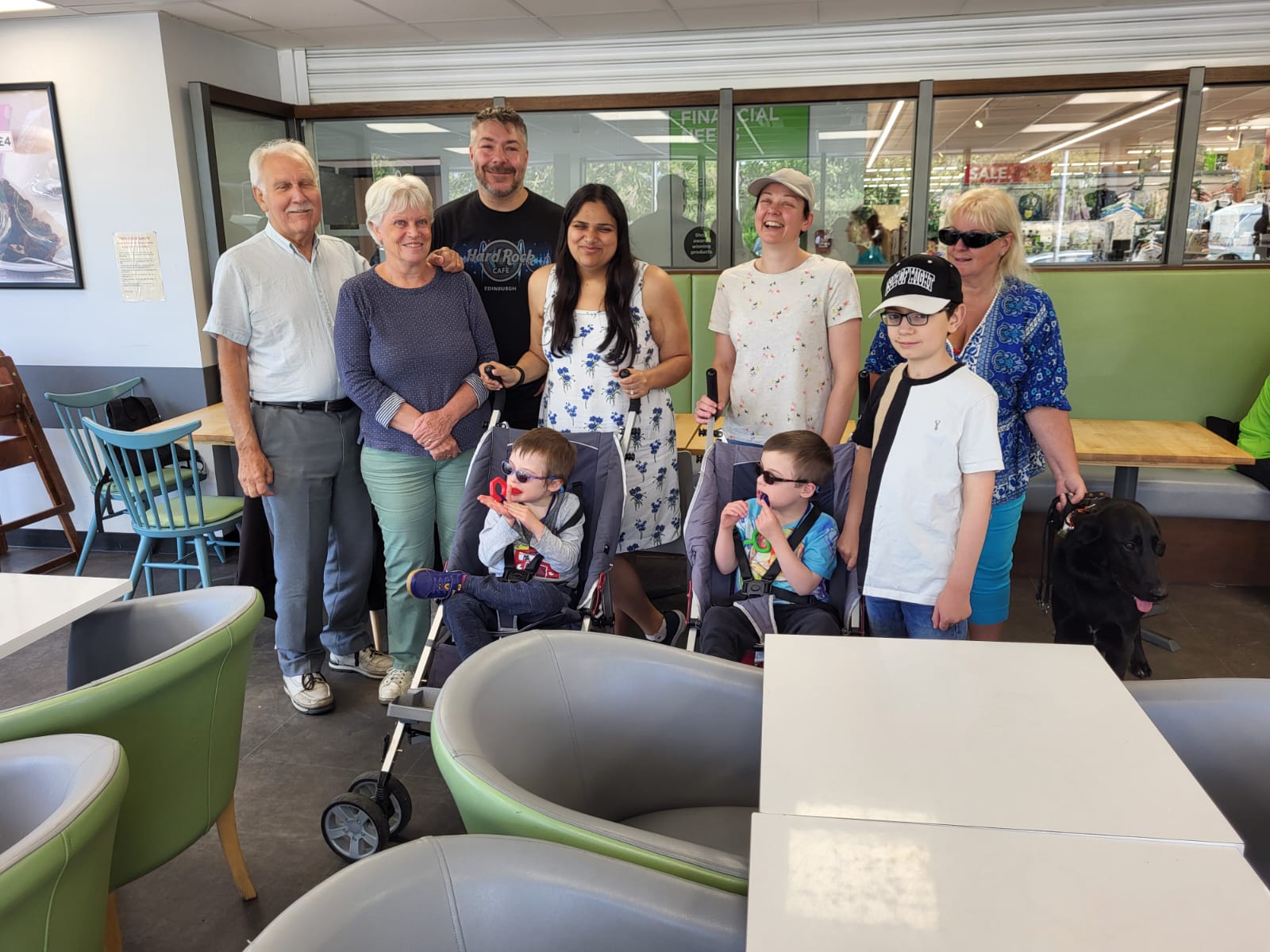 a group of people standing in a line and smiling at the camera. There are two kids in prams