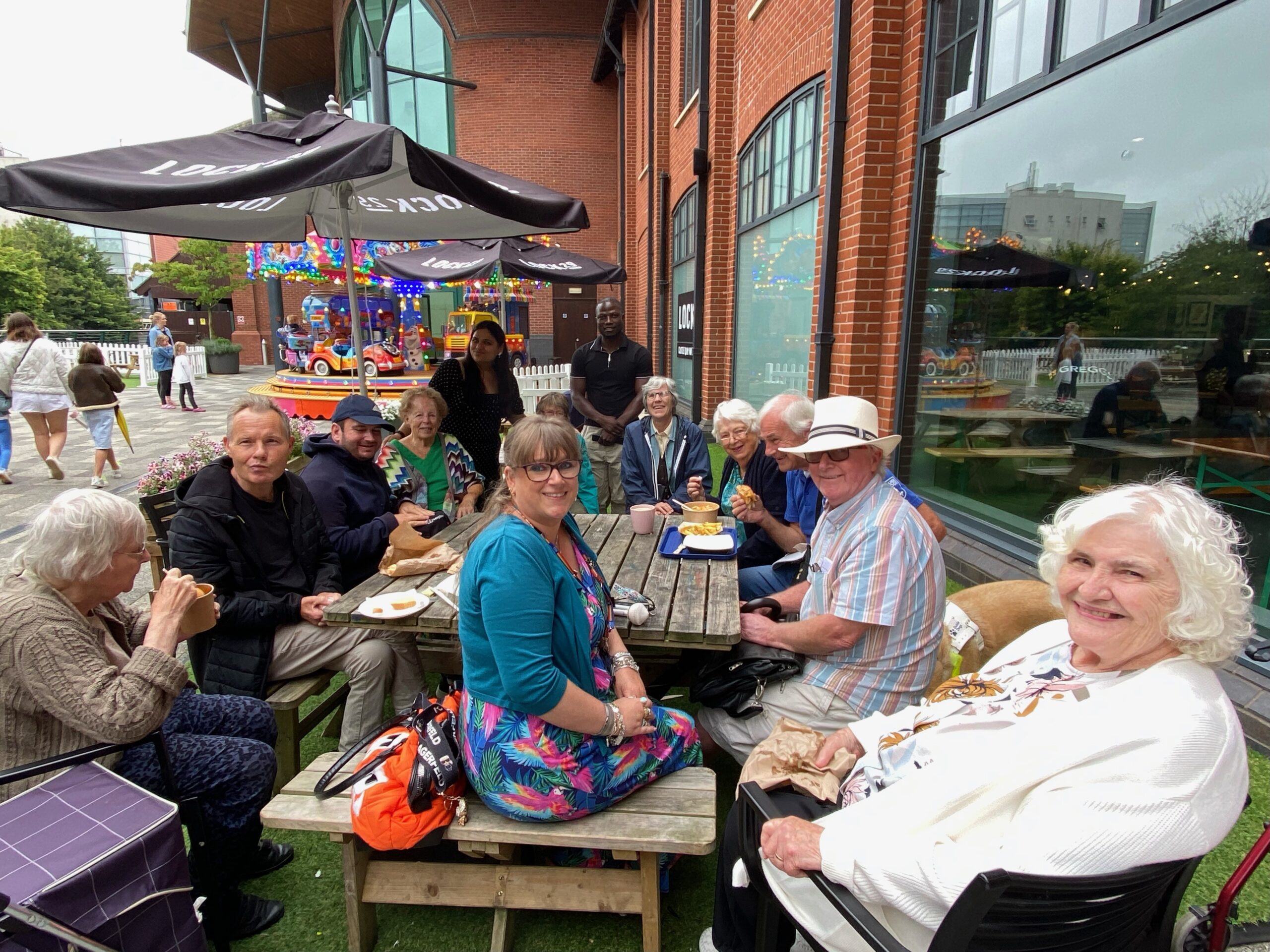 a group of people sitting around a table outside and smiling at the camera