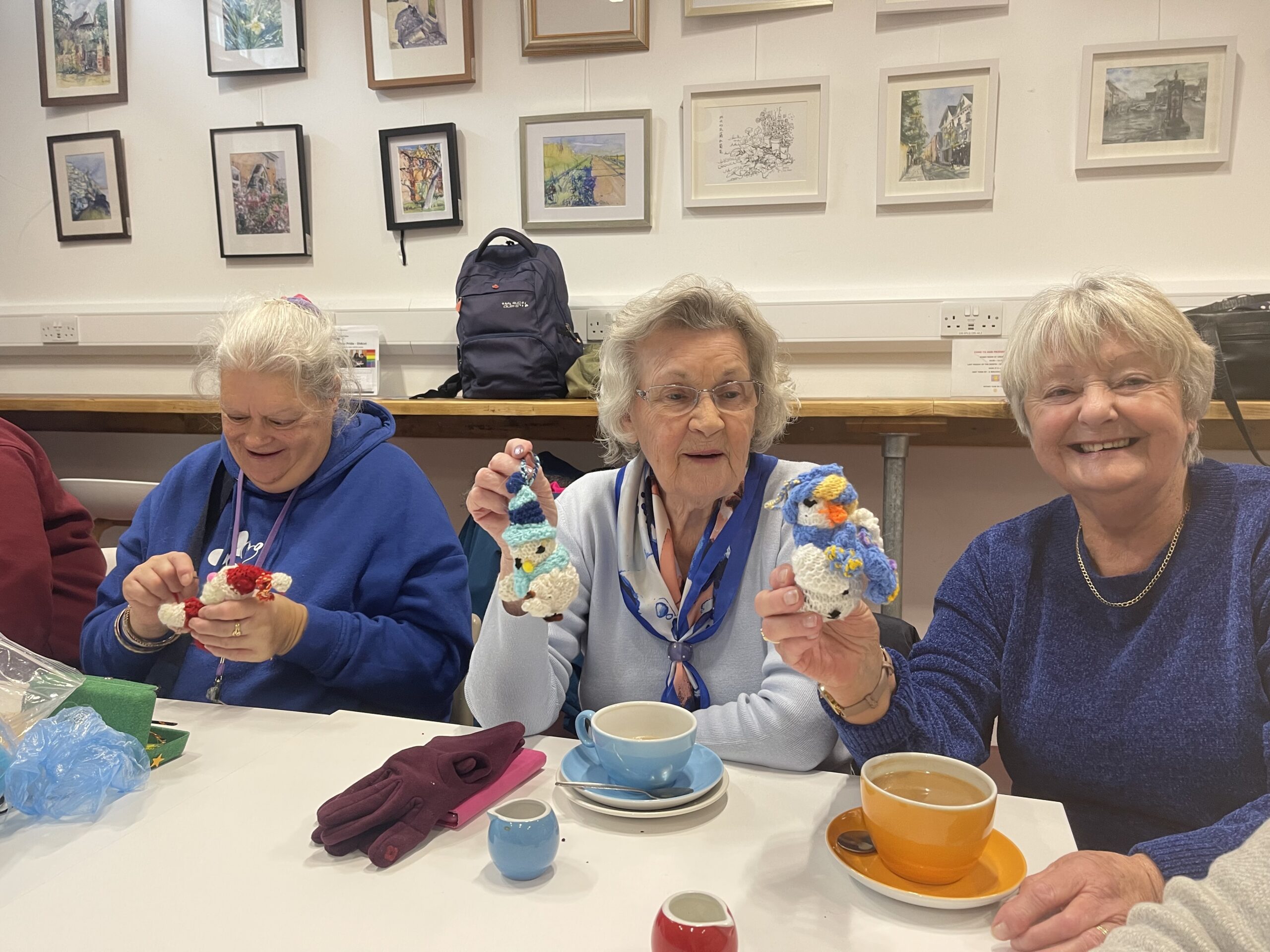 three women showing the camera what they have knitted